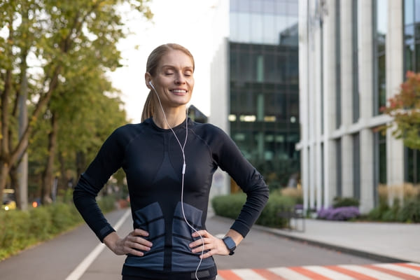 Eine sportliche Frau mittleren Alters steht nach einem Ausdauerlauf entspannt und ohne Stress da, Augen geschlossen